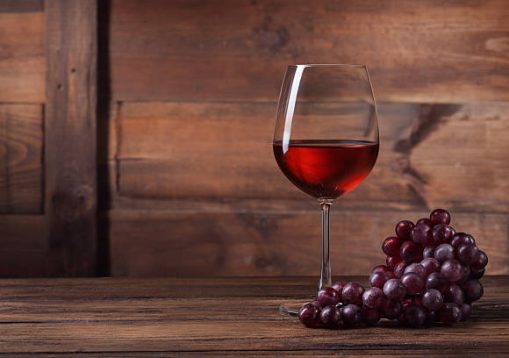 Red wine in glass with grape on wooden background